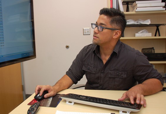 Information Technology Analyst II Jonathan Penaflor work on a computer in a conference room.