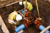 Crew members lower a new water main tee into the ground.