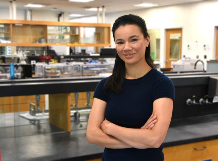 Kristy Fournier stands facing the camera with lab in back