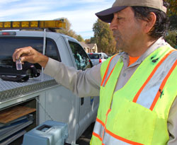 Water utility worker, standing by pickup truck, looks at water sample in small bottle.